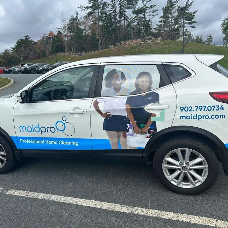 White MaidPro car with professional home cleaning advertisement showing two women and contact details on side.