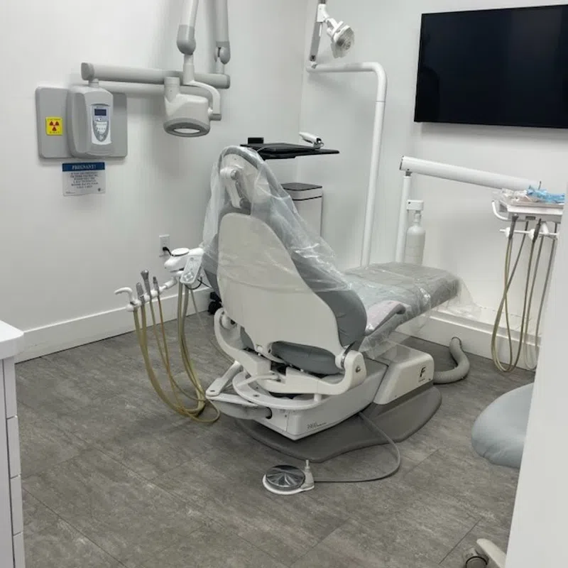 Modern dental clinic with a dental chair, overhead light, equipment, and a wall-mounted TV screen.