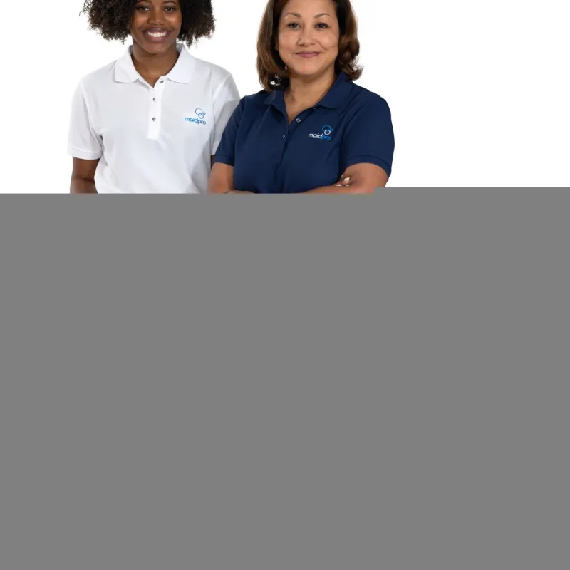 Two smiling women wearing MaidPro uniforms with polo shirts and aprons standing on white background.