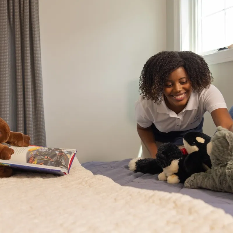 Smiling woman arranging stuffed animals on bed in cozy bedroom with natural light from window