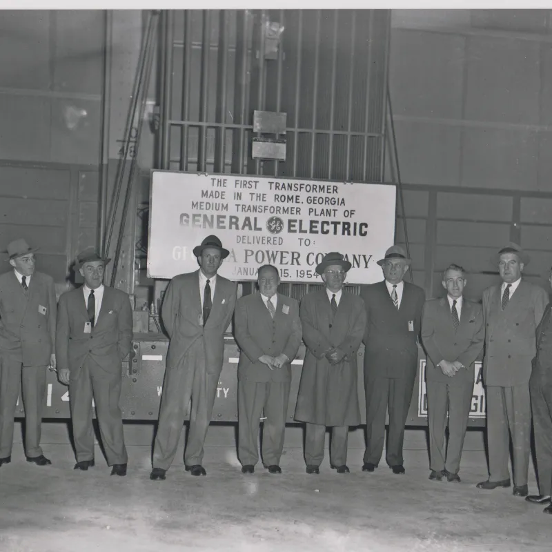 Group of men in suits and hats stand in front of sign for first General Electric transformer in Rome, Georgia, 1954.