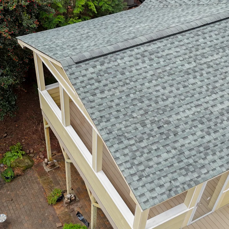 Aerial view of a house roof with gray asphalt shingles and a balcony overlooking a garden patio in Marietta