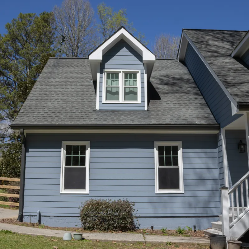Blue house exterior with white trim, dormer window, porch, and a wooden fence under clear sky in Atlanta