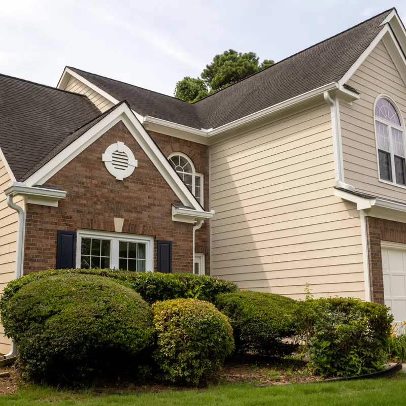 A two-story brick and beige siding home with a black asphalt shingle roof designed to withstand Marietta GA humidity damage siding replacement services in Marietta by Nelson Exteriors.