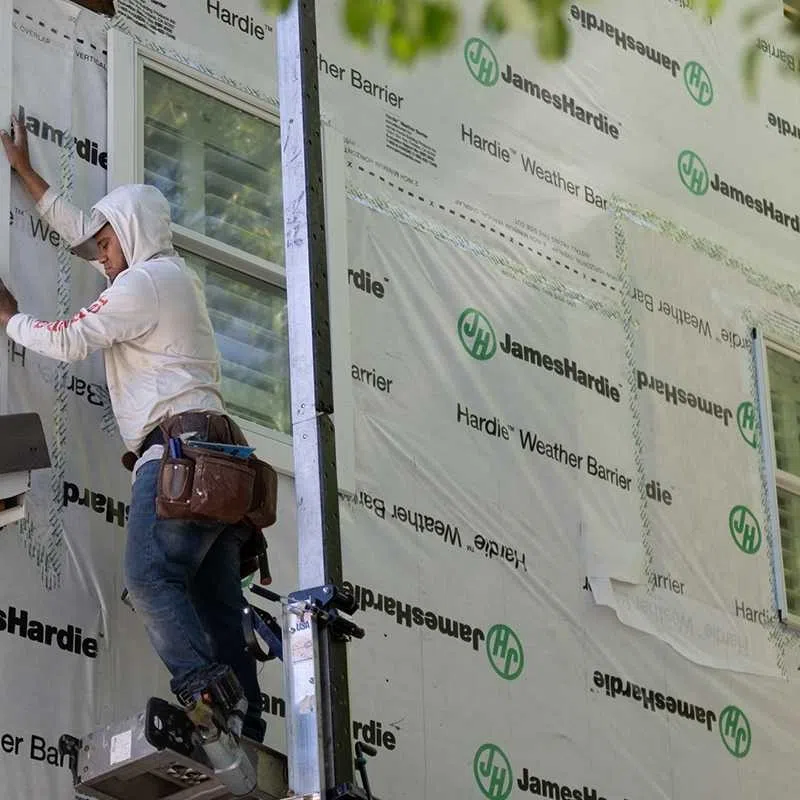 Construction worker installing window on house wrapped in James Hardie Weather Barrier sheeting.