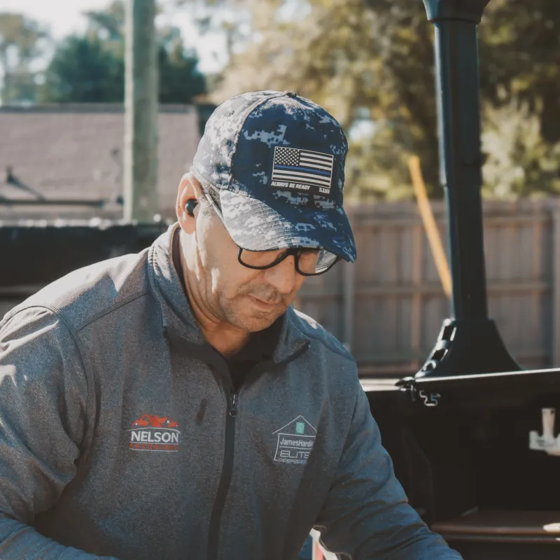 Man in cap and glasses working outdoors with paint cans and tools on a sunny day.