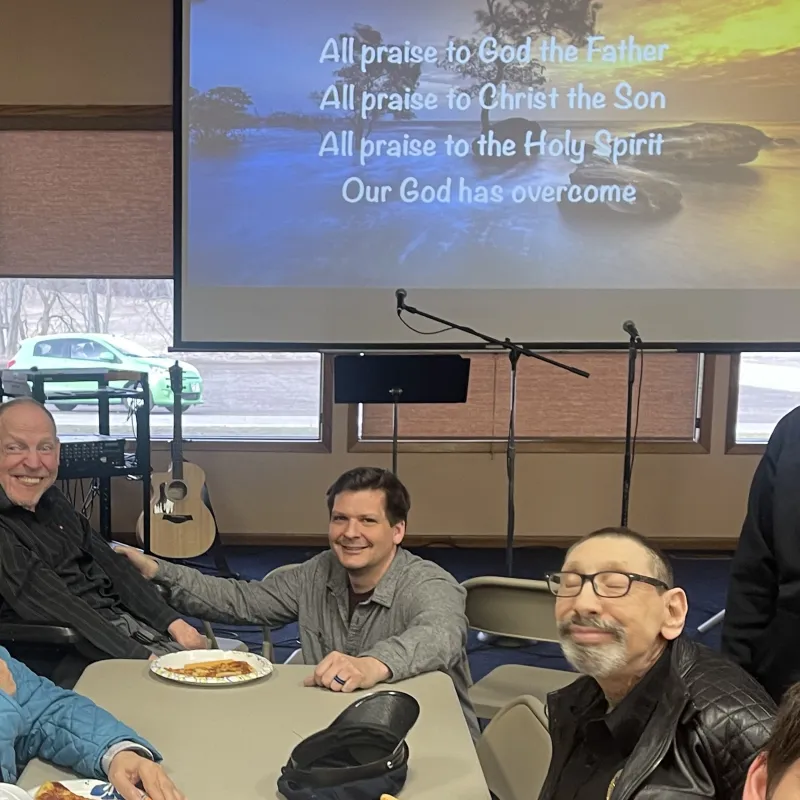 Benny Hill et al. sitting at a table with a screen behind them