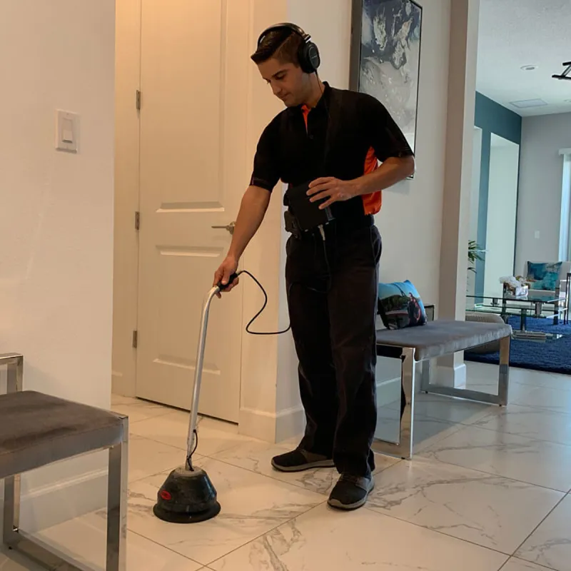 Technician wearing headphones using equipment to inspect or detect under white tiled floor in a modern living room