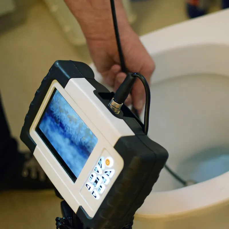 Plumber using a video inspection camera to check inside a toilet bowl and drain for blockages or damage.