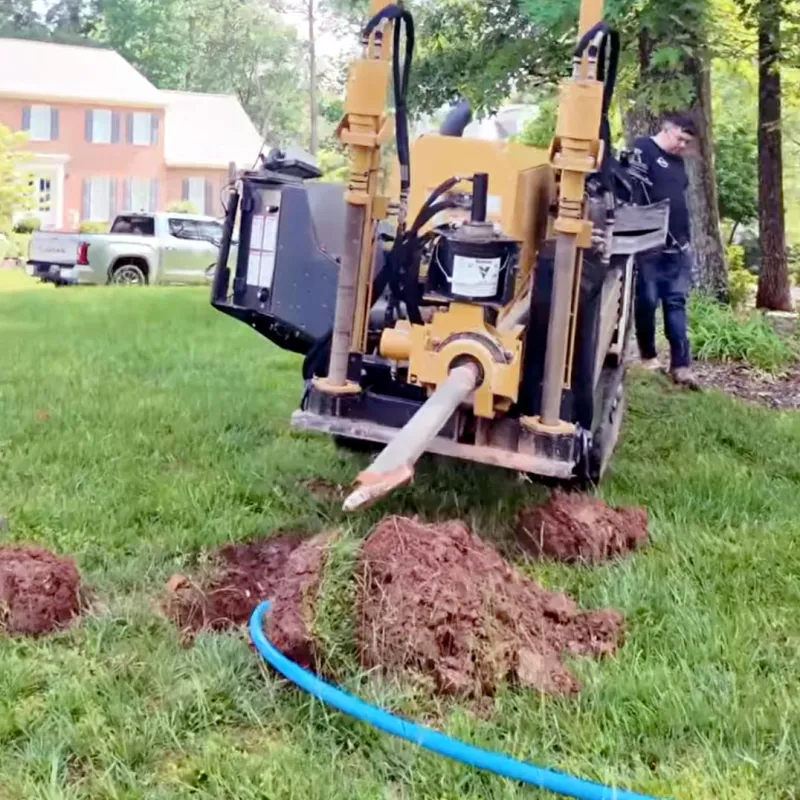 Horizontal directional drilling machine digging underground near residential house with worker and green trees