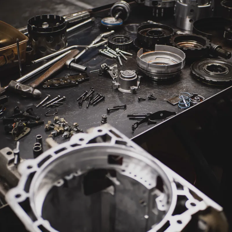 Disassembled mechanical transmission parts and tools spread out on a metal workbench in a workshop.
