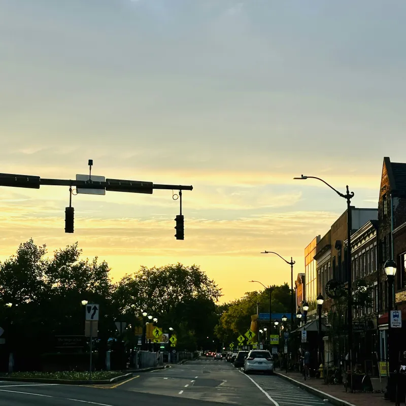 Quiet urban street at sunset with traffic lights, parked cars, street lamps, and buildings along the road.
