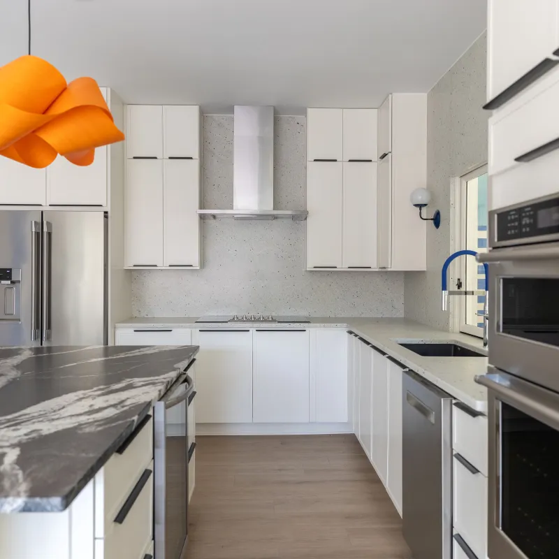 Modern white kitchen with marble island, stainless steel appliances, and an orange pendant light fixture