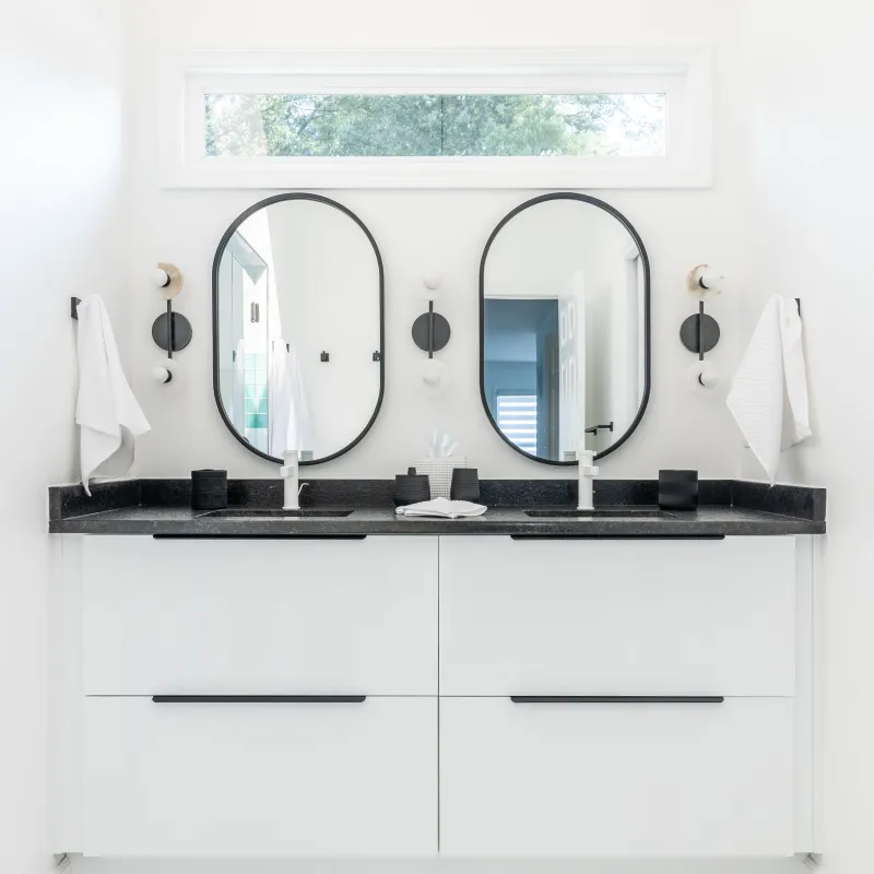 Modern white bathroom with double black-framed mirrors, black countertop, and minimalistic decor under a narrow window.