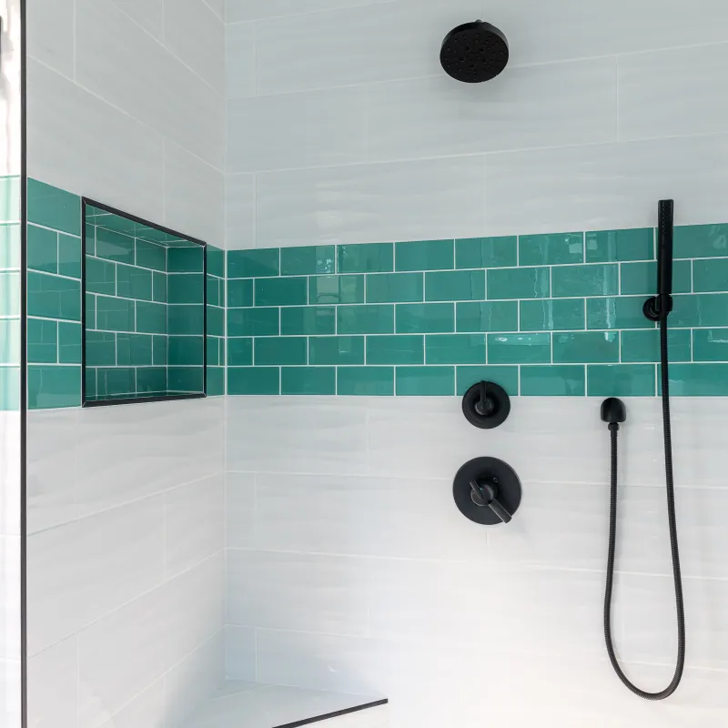 Modern shower with white and teal tiles, black fixtures, built-in bench, and recessed shelf in bathroom.