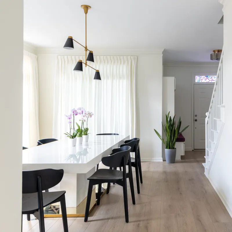 Modern dining area with a white table, black chairs, orchids, wood flooring, and natural light from large windows.
