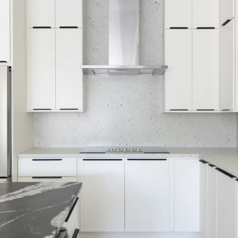 Modern white kitchen with sleek cabinetry, stainless steel refrigerator, black marble island, and minimalist design.