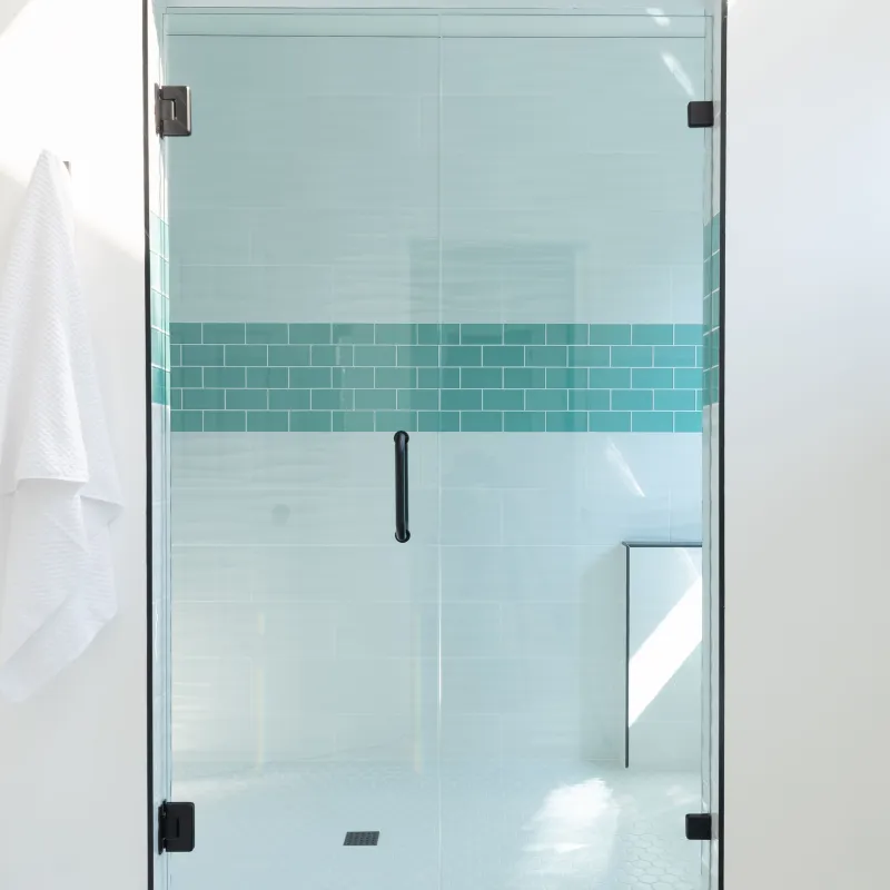Modern glass shower enclosure with blue tile accent and white hexagon floor tiles in bright bathroom