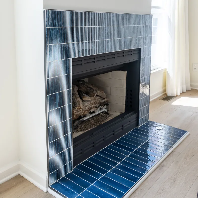 Modern fireplace with blue tiled surround and hearth in a bright room with light wood flooring.