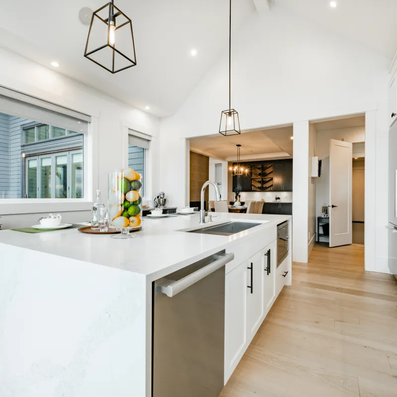 Modern bright kitchen with white island, stainless steel appliances, pendant lights, and wooden flooring