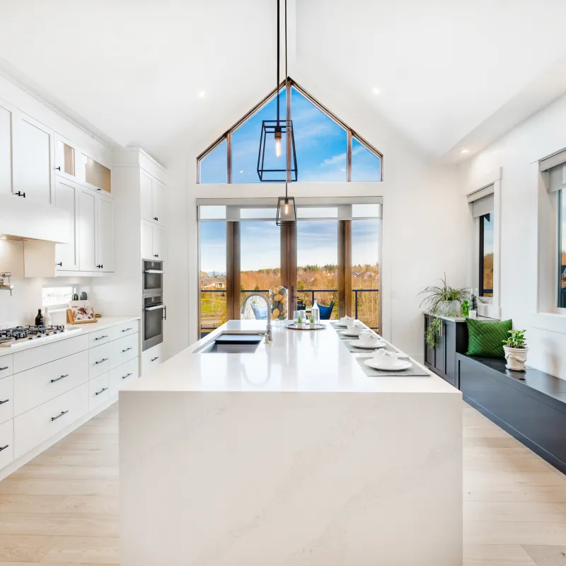 Bright modern kitchen with white cabinetry, large island, pendant lights, and expansive windows with outdoor views
