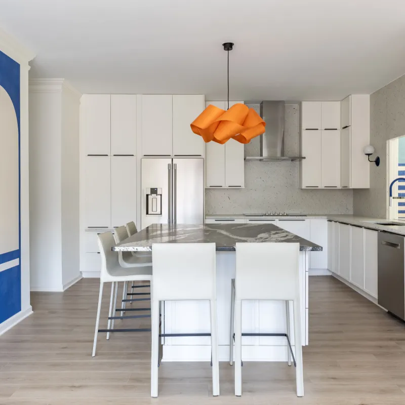 Modern white kitchen with marble island, orange pendant light, stainless steel appliances, and blue geometric wall art