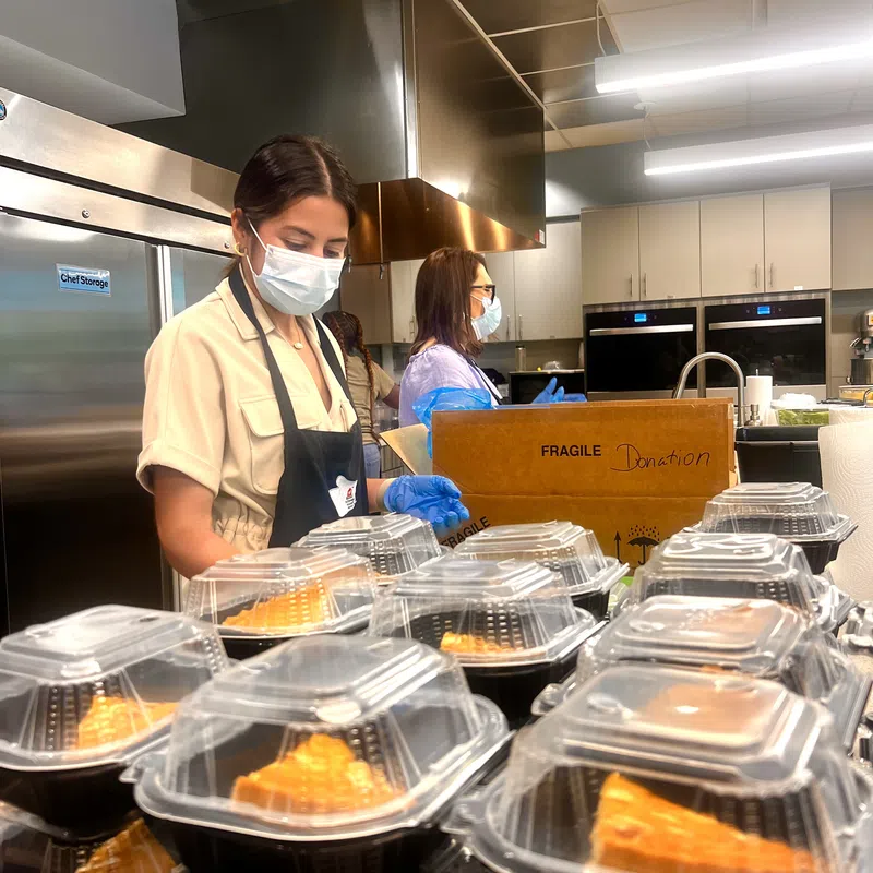 Volunteers wearing masks and gloves packing pie slices in plastic containers in a kitchen for donation.