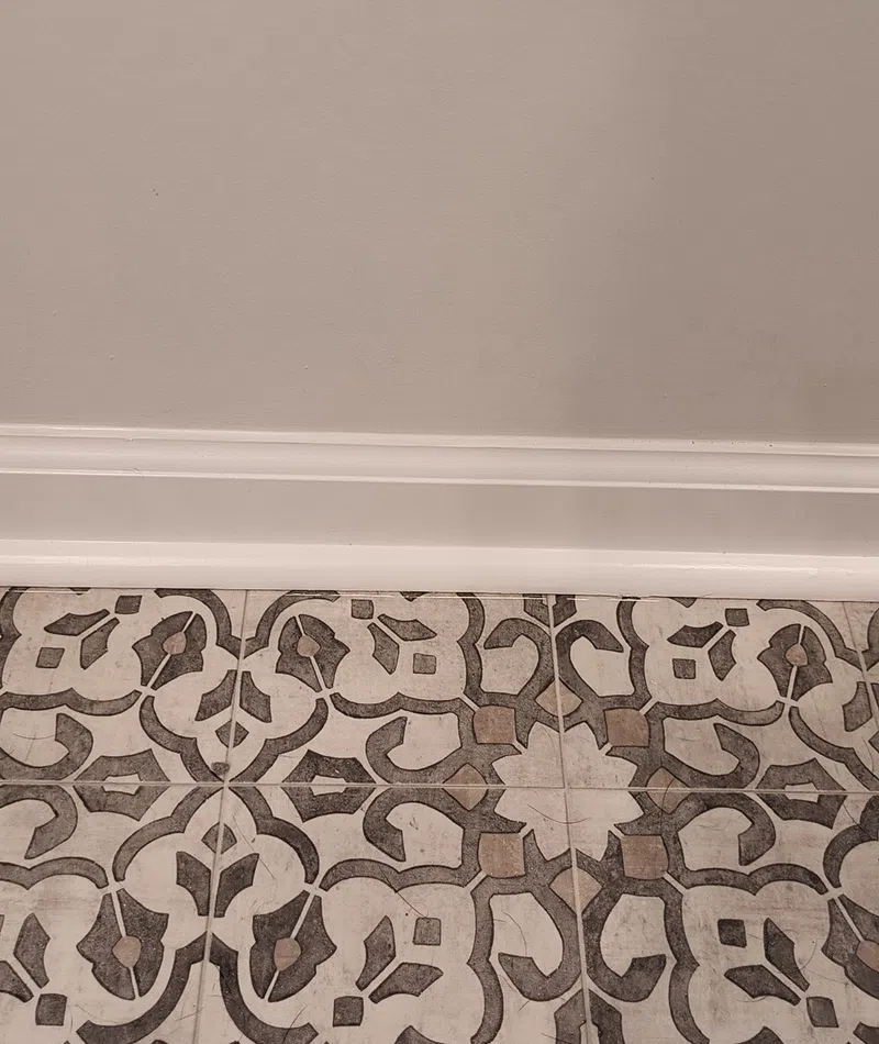 Decorative patterned floor tiles with geometric and floral motifs next to a white baseboard and beige wall.