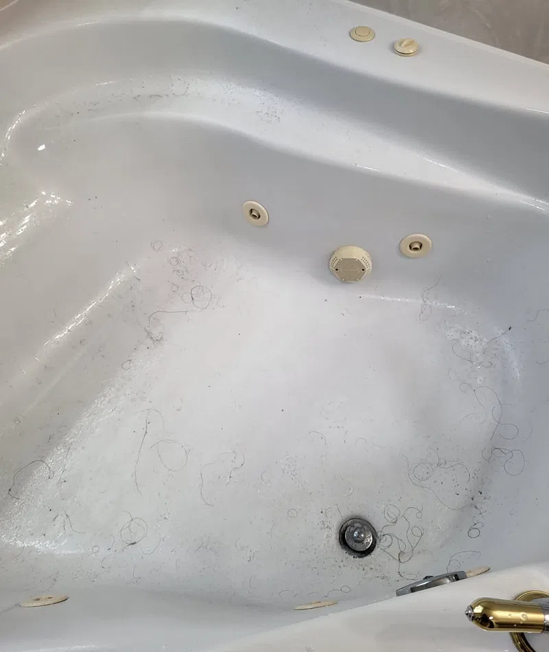 Dirty white bathtub with visible hair strands and grime around the drain and jets.