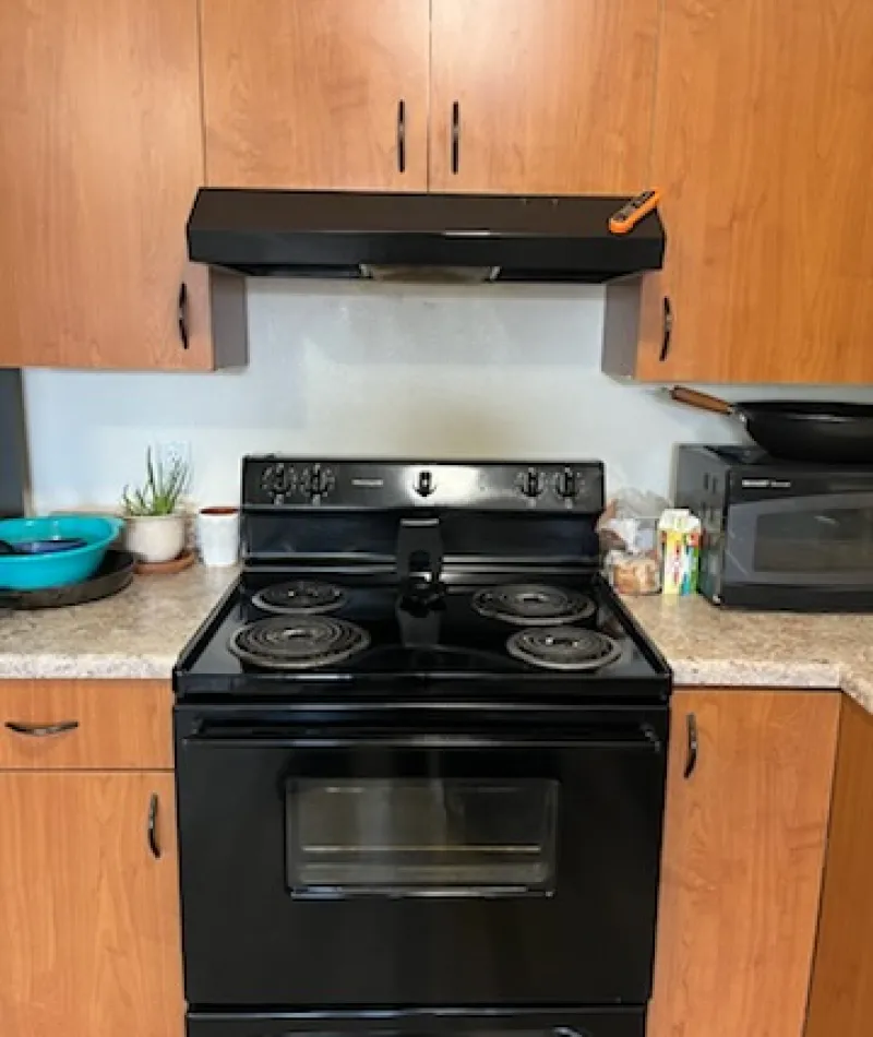 A black stove in a wooden kitchen with a microwave and cooking utensils on the countertop.