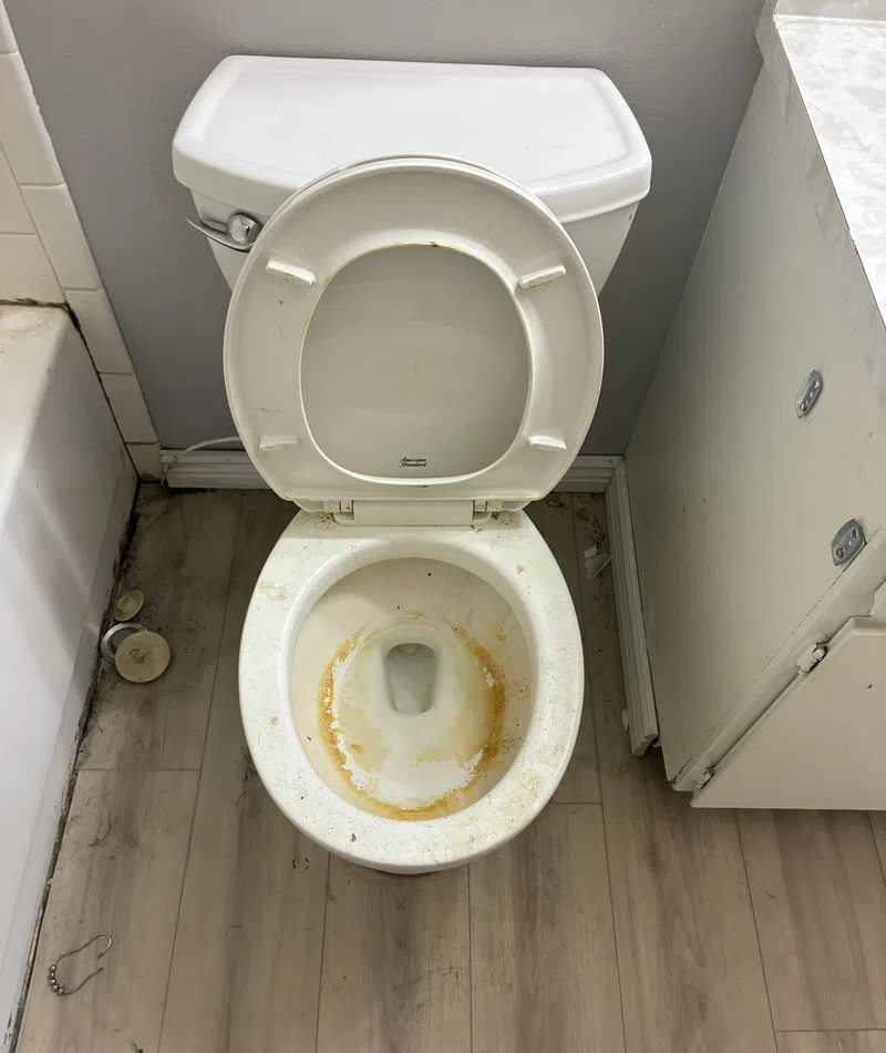 Top view of a stained, dirty white toilet bowl with open lid in a bathroom with wood flooring.
