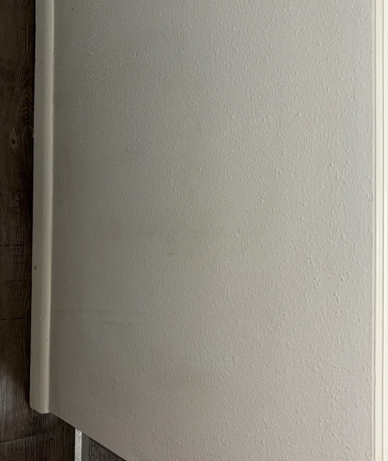 Close-up of a textured beige wall meeting dark wooden flooring and white baseboard trim in a corner.