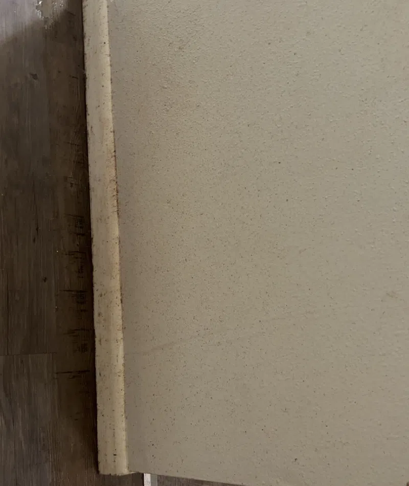 Close-up of a textured beige wall meeting dark wood flooring and tiled floor with a white baseboard.
