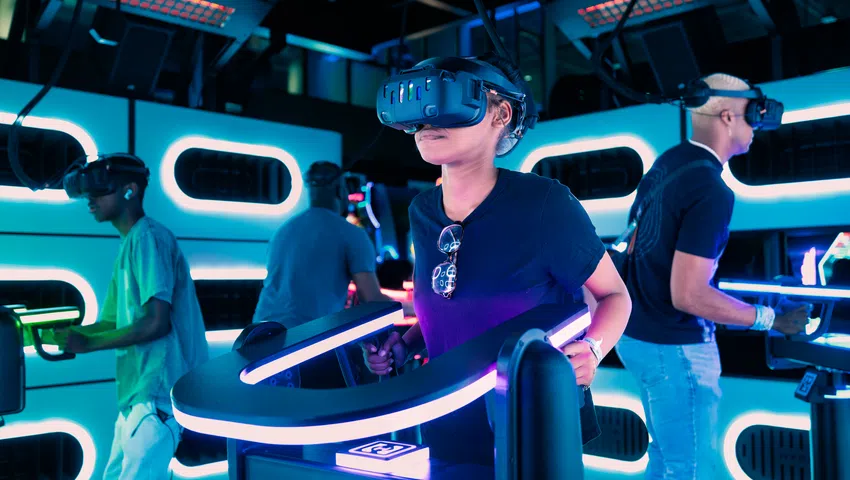 People experiencing virtual reality games using VR headsets and interactive motion controllers in a neon-lit arcade.