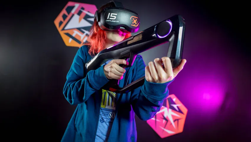 Person wearing Limitless VR headset holding a futuristic black VR gun with neon purple lights in a gaming setup.