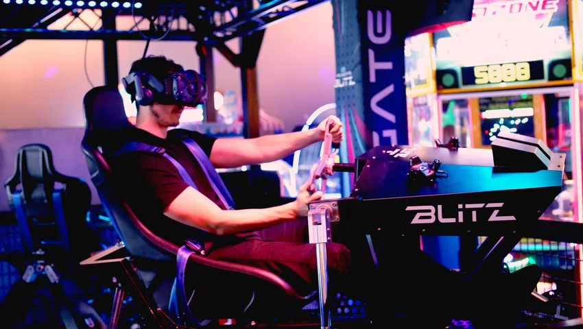 Person enjoying a VR racing simulator in an arcade with vibrant lights and gaming setup.