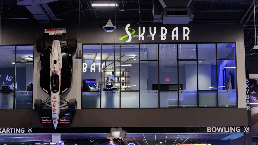 Indoor entertainment center with a race car mounted on the wall and neon-lit arcade games below.