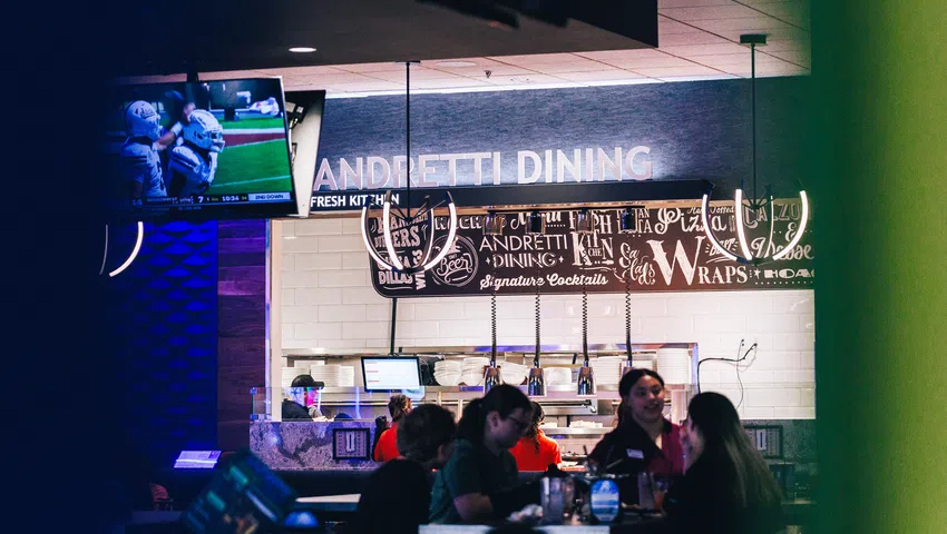 Customers dining inside Andretti Dining area with a TV showing a sports game in the background.