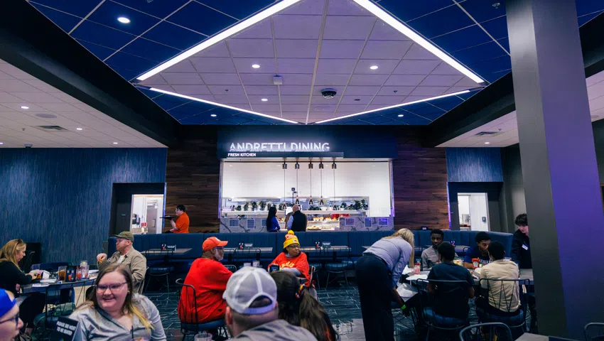 People dining and socializing in a modern restaurant with blue and wood interior and geometric ceiling lights.