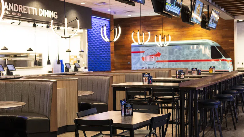 Modern dining area with wooden tables, high stools, booth seating, pendant lights, and televisions above the bar.