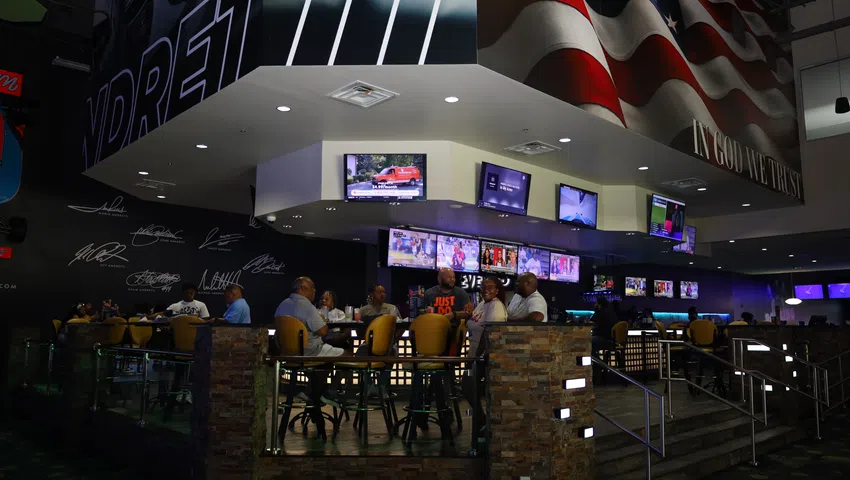 Sports bar interior with patrons seated around tables, multiple TVs displaying sports, and patriotic decor.