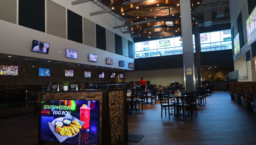Spacious sports bar interior with multiple TVs, wooden tables, modern lighting, and a promotional Southwest egg roll sign.