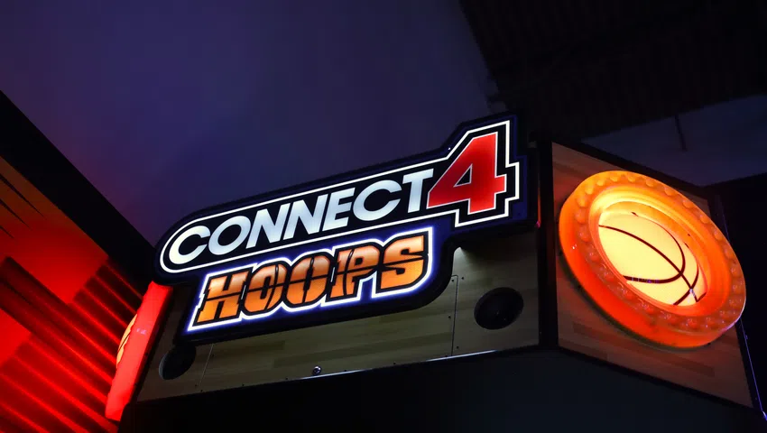 Illuminated arcade game sign for Connect 4 Hoops with a glowing basketball hoop and dark background.