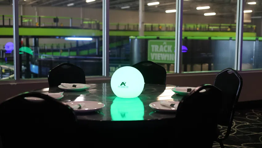 Round dining table set with plates and napkins around glowing green orb in indoor recreational facility.