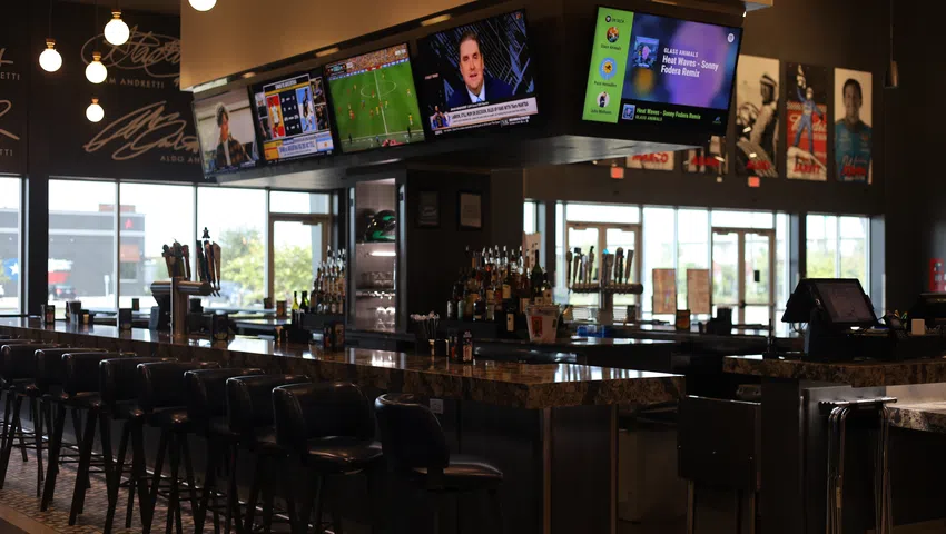 Modern sports bar interior with multiple TVs, bar stools, and ambient hanging lights during daytime.