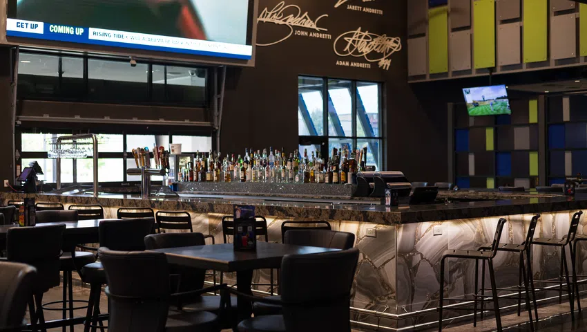 Modern sports bar interior with marble bar counter, stools, tables, and large TVs mounted on walls.