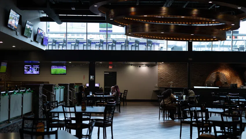 Spacious modern sports bar with high ceiling, multiple TVs, wooden tables, and a large circular chandelier.