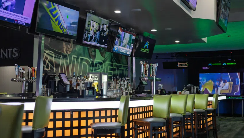 Modern sports bar with multiple TVs, illuminated bar counter, green high stools, and sports memorabilia decor