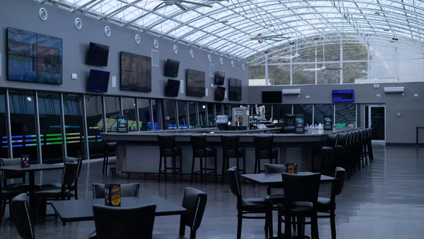 Modern sports bar interior with multiple TVs, black chairs, tables, and a curved bar under a glass ceiling.