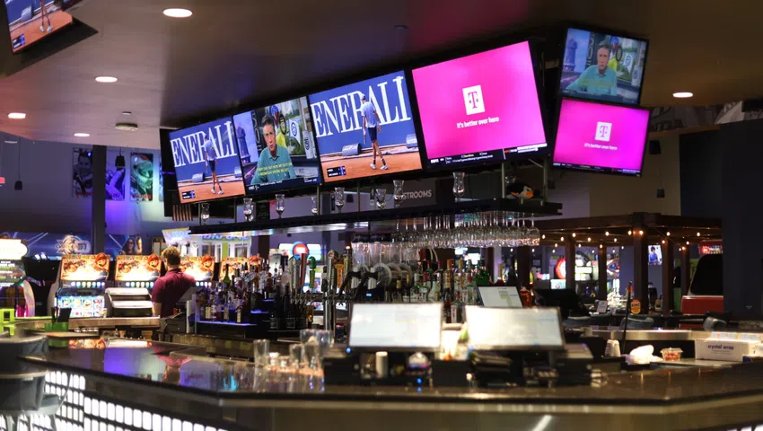 Modern bar interior with multiple TVs showing sports and advertisements above the counter and drinks on display